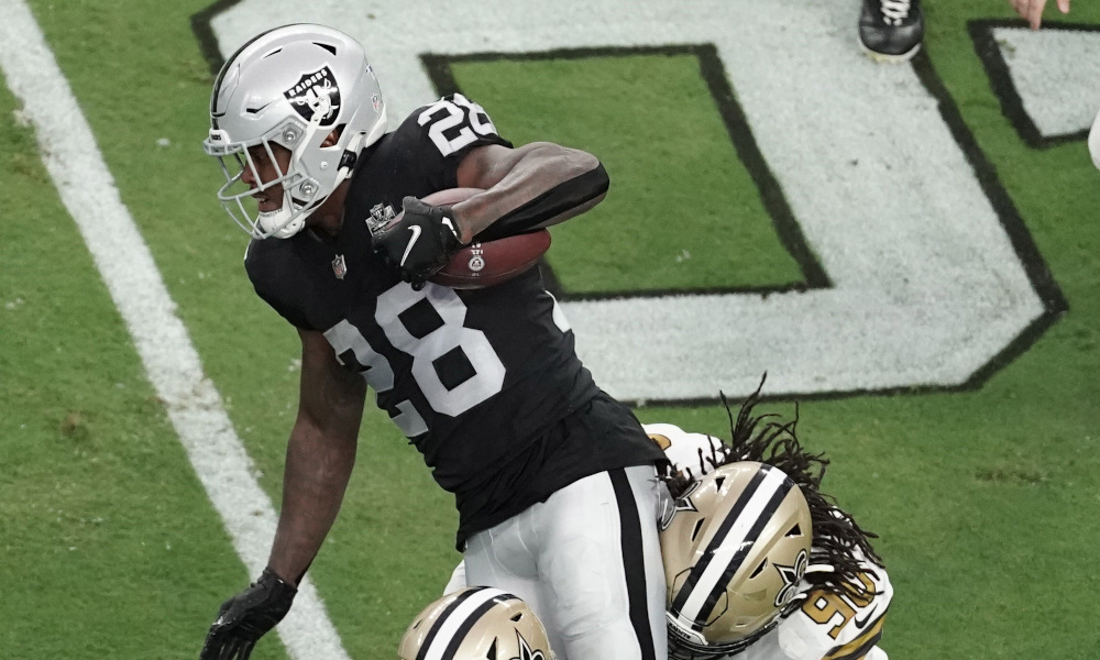 Josh Jacobs of Raiders runs the ball through two Saint defenders