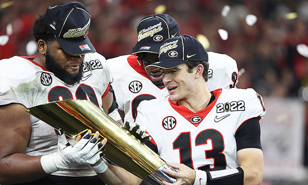 Stetson Bennett (#13) holding 2022 CFP National Championship Trophy with Georgia teammates